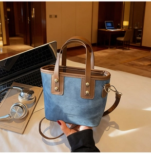 Détail du cabas en jean bleu avec anses en cuir marron et logo de mode sur surface blanche