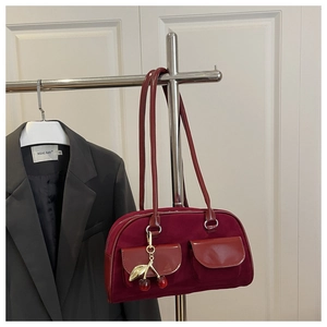 Detail view of burgundy suede shoulder bag featuring front pockets and cherry pendant accessory