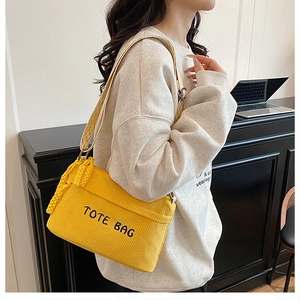 Detail of yellow corduroy tote bag with black embroidery and woven strap worn crossbody