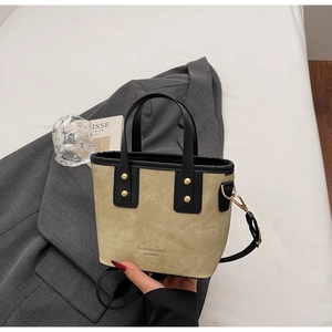 Détail d'un sac seau kaki avec poignées noires et clous dorés sur fond de veste