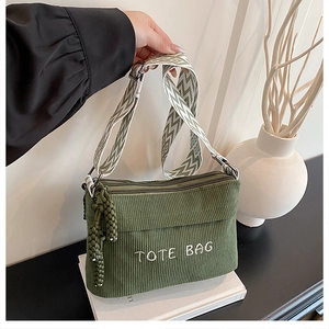 Detailed close-up of dark green corduroy tote bag with embroidered letters and woven strap