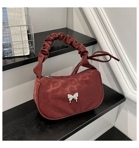 Detail of burgundy ruched handbag with silver butterfly clasp on monochrome display