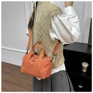 Detail of a bright orange nylon cylinder bag featuring adjustable crossbody straps