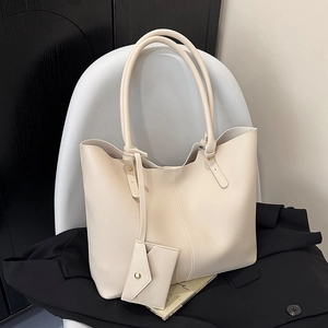 Minimalist beige large capacity tote bag with matching envelope pouch on a modern chair