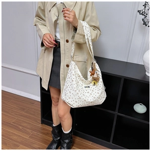 Close-up of white corduroy bag with brown bow prints, teddy bear charm, and adjustable strap