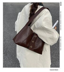 Dark brown leather shoulder bag with gold metal eyelets shown on a model outdoors