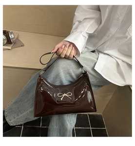 Détail d'un sac à bandoulière en cuir verni chocolat avec un nœud métallique doré chic