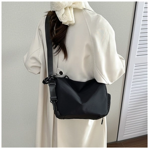 Vista trasera detallada de un bolso bandolera de nailon negro llevado con una gabardina beige