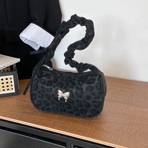 Leopard print underarm bag with ruched handle and silver butterfly charm on wooden table