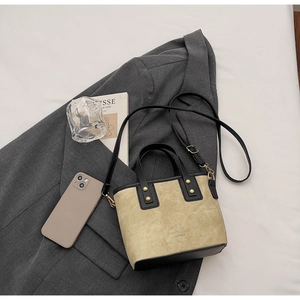 Détail d'un sac bandoulière en cuir kaki avec rivets dorés sur fond de blazer gris