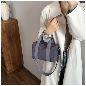 Close-up of dark grey nylon boston bag with round metal logo and woven shoulder strap