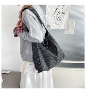 Detail of checkered tote bag showing wide shoulder strap and side brand tag for comfort