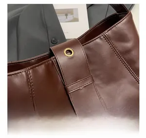 Detail view of dark brown leather handbag featuring vertical stitching and golden eyelets