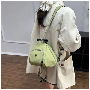Mochila pequeña de nailon verde aguacate llevada por una modelo en una sala sobria