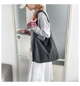 Detail view of the large black and grey plaid tote bag worn over the shoulder by a model