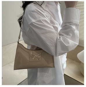 Détail du sac hobo en cuir verni beige avec boucle nœud doré porté sur l'épaule