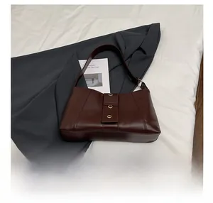 Detail view of dark brown leather underarm bag with decorative metal rings and phone inside