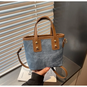 Détail d'un sac cabas en denim bleu avec anses en cuir marron et rivets dorés