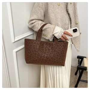 Detail of large brown leopard print tote bag in matte leather being held by a model