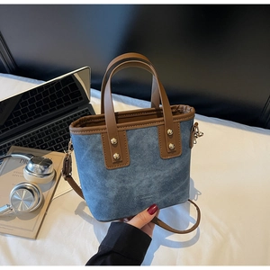 Gros plan sur un sac seau en denim bleu avec anses en cuir marron et rivets dorés