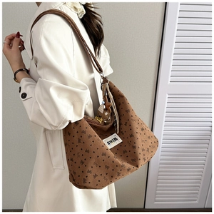 Detail view of brown corduroy tote bag with heart prints and plush bear charm on model