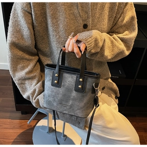 Détail du sac seau gris avec anses noires, rivets dorés et bandoulière amovible