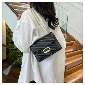 Detail of black quilted shoulder bag with V-stitch pattern and gold chain strap