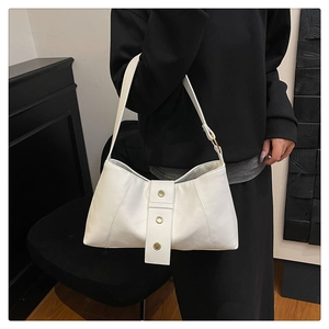 Detail of white leather shoulder bag featuring vertical strap and golden metal eyelet accents