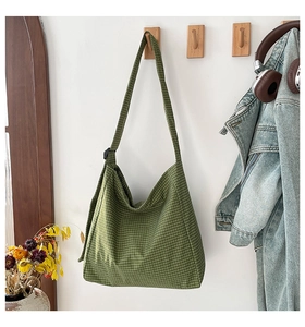 Detail of green and beige plaid canvas tote bag hanging on wooden hook in a room