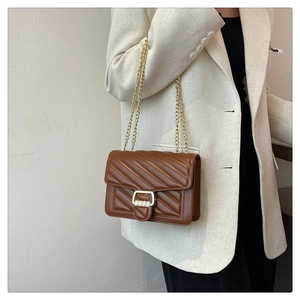 Detail of a brown quilted leather crossbody bag with gold chain strap and metal lock
