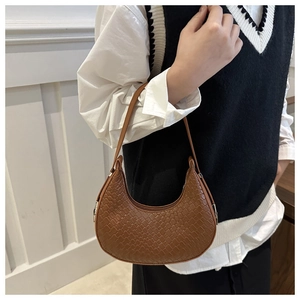 Detail of caramel brown woven leather crescent shoulder bag styled on a female model