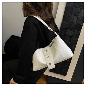 Detail of white leather shoulder bag featuring three large gold metal grommets on strap
