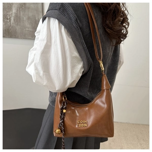 Vue détaillée d'un sac demi-lune marron avec des lettres dorées et un charme tressé élégant
