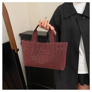 Detail of a vintage burgundy leopard print tote bag held by a person in a black coat