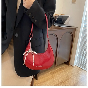 Detail view of red glossy crescent shoulder bag with pearl bow charm and logo
