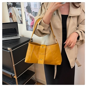 Detail view of yellow leather baguette bag featuring stylish golden rivets and a shoulder strap