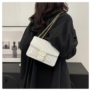 Detail of white quilted crossbody bag with gold chain strap shown on person
