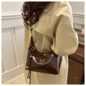 Détail du sac croissant en cuir ciré marron foncé avec logo doré et pendentif décoratif