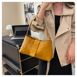 Detail of yellow faux leather shoulder bag with gold metal eyelets on a modern model