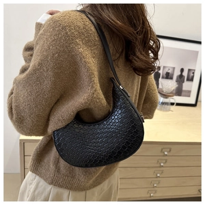 Detail of black faux leather crescent bag with woven texture worn by a model