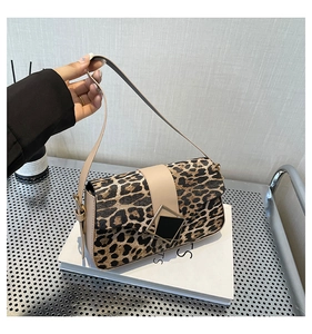 Close-up of leopard print shoulder bag with gold-trimmed buckle on leather surface