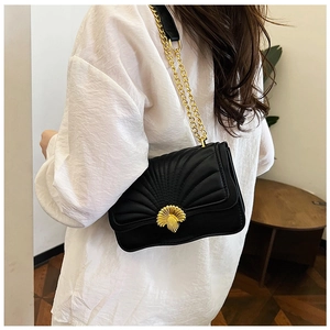 Macro view of black quilted crossbody bag with golden shell-shaped rotary clasp