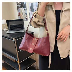 Detail of burgundy shoulder bag featuring metallic gold eyelets on a decorative strap