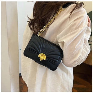Detail shot of black quilted bag with golden shell-shaped lock on a model shoulder