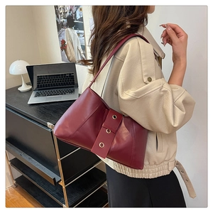 Detail view of burgundy minimalist shoulder bag with gold metal eyelets on wide buckle strap