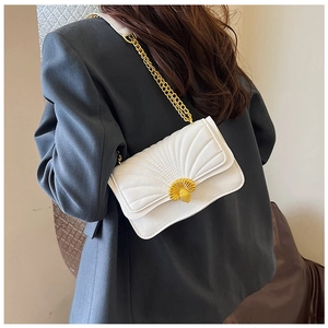 Detail of white quilted crossbody bag featuring a golden scallop-shaped metal lock and chain strap