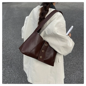 Detail of dark brown leather shoulder bag with gold metal eyelets and folded texture