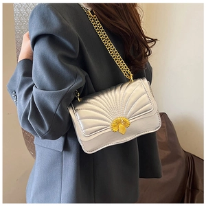 Detail of silver quilted crossbody bag with golden shell clasp and chain strap