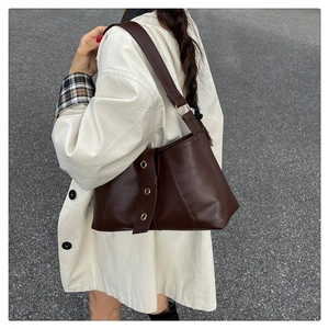 Detail view of a vintage dark brown leather shoulder bag with gold metal studs on the side