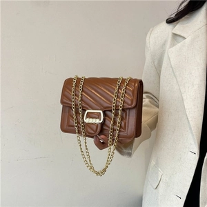 Brown quilted crossbody bag with V-stitch design and gold chain strap on woman